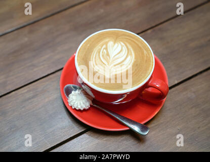 Piatto bianco caffè con modello cuore in un bicchiere di rosso sul tavolo di legno Foto Stock