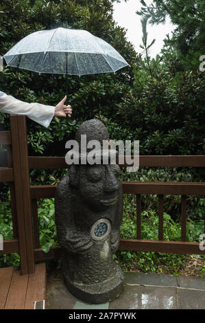 Jeju Island, Corea del Sud, settembre 08, 2019: mans mano trattiene il suo ombrello oltre Dol Hareubang statua sul giorno di pioggia Foto Stock