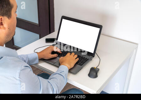 Persona che lavora su un computer portatile in un ufficio business ambiente. Oltre la spalla shot di man digitando su un computer con schermo vuoto. Foto Stock