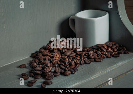 I chicchi di caffè & tazza vuota sul rustico verniciato grigio ripiano. Foto Stock