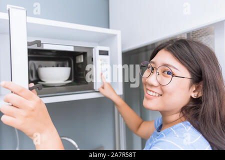 Girl Teen sorridente riscaldare il cibo usando un forno a microonde con  vetro ceramica ciotola Foto stock - Alamy