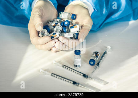 Dottore in un blu camici chirurgici e maschera e tiene in mano le bottiglie con insulina per il diabete. Molte le siringhe e farmaci per iniezione sul tavolo bianco Foto Stock