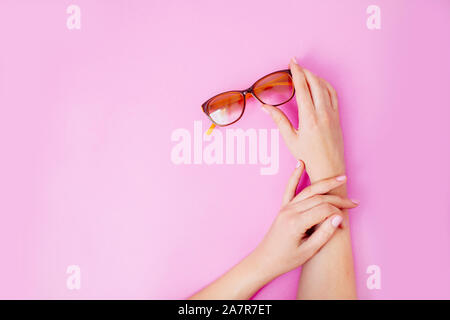 Mani femminili tenendo delicatamente i bicchieri su un pastello sfondo rosa. Foto Stock