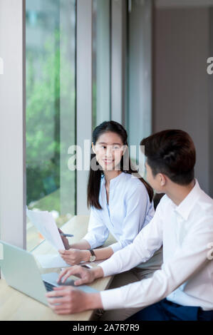 Vita fino colpo di due sorridente giovane maschio e femmina gli imprenditori con i capelli neri parlare insieme mentre si lavora a una scrivania in un ufficio Foto Stock
