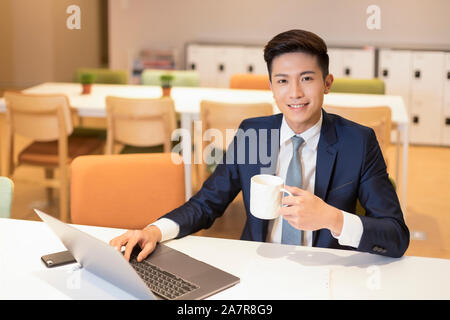 Vita fino colpo di un giovane imprenditore con i capelli neri e tuta guardando la telecamera tenendo premuto il caffè Foto Stock