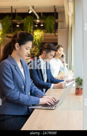Un gruppo di tre giovani maschi e femmine imprenditori lavora ad una scrivania in un ufficio con la donna in primo piano utilizzando un computer portatile Foto Stock