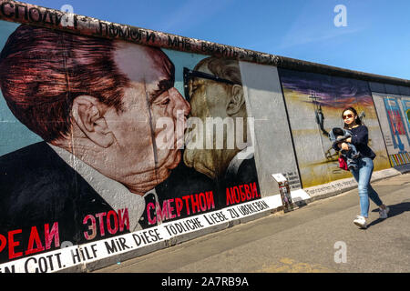 Muro di Berlino, giovane donna asiatica che passa intorno East Side Gallery, Brezhnev Honecker Kiss Germania Friedrichshain città strada Foto Stock