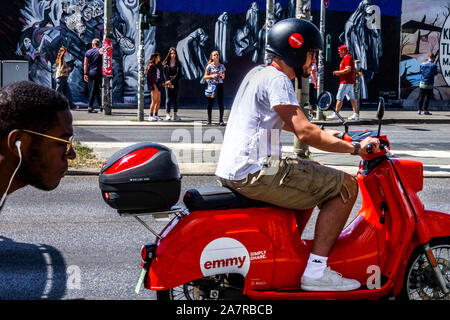 Berlino muro, un uomo a noleggio scooter Emmy passando a Muhlenstrasse, East Side Gallery Germania Friedrichshain città strada Foto Stock