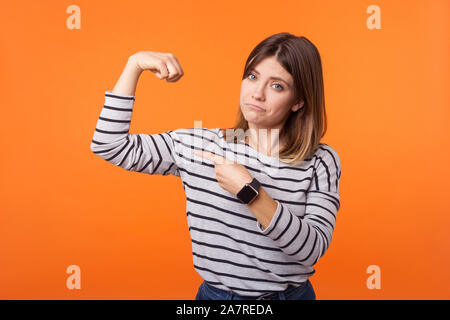 Ritratto di orgoglioso fiducioso donna con capelli castani a manica lunga camicia a righe di salita del braccio pointng al bicipite, vantando di potere femminile, il femminismo. indo Foto Stock