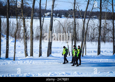Un gruppo di poliziotti canadese di pattuglia durante il periodo invernale. Gli ufficiali di polizia nella missione di indagine nei pressi di un fiume congelato. Foto Stock