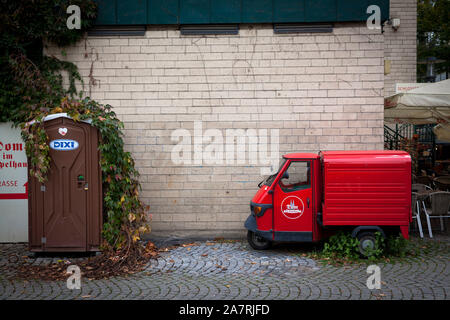 Portable Dixi wc e un Ape Piaggio veicolo commerciale leggero nella parte vecchia della città di Colonia, Germania. Dixi Klo und Piaggio Ape Kleintranspor Foto Stock