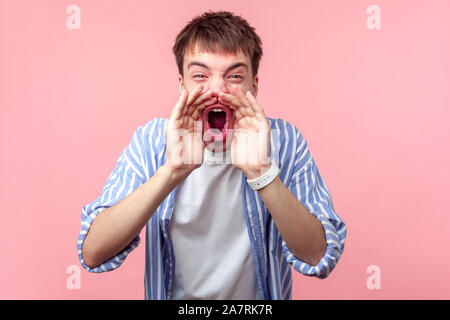 Annuncio! Ritratto di aggressivo furious i capelli castani uomo nel casual striped shirt mantenendo le mani vicino a bocca spalancata e urlando, gridare le cattive notizie Foto Stock