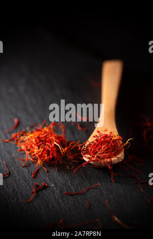 Lo zafferano essiccato spice in cucchiaio di legno sul nero ardesia sfondo. Foto Stock