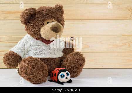 Toy marrone orsacchiotto siede su un bianco tavolo di legno su uno sfondo di tavole di legno Foto Stock