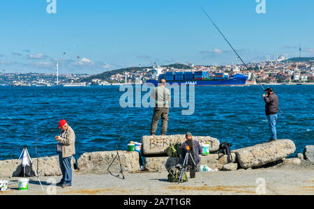 ISTANBUL Turchia i pescatori sulle rive del Bosforo CON IL PASSAGGIO DI UN CONTENITORE GRANDE NAVE Foto Stock