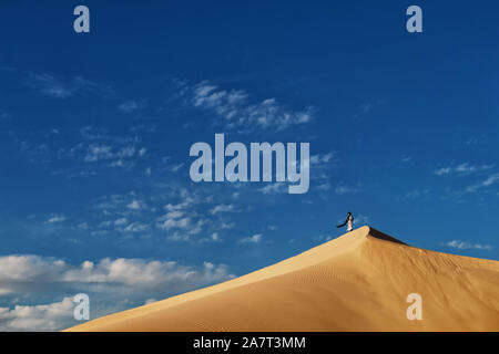 Un tradizionale vestito uomo marocchino sorge su una duna di sabbia contro un nuvoloso cielo blu, il deserto del Sahara, Marocco. Foto Stock