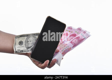 Una mano che tiene un telefono cellulare vicino al yuan e dollaro banconote Foto Stock