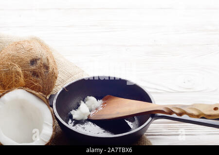 Noce di cocco, shell con carne, padella in ghisa e la spatola sulla canapa sacco su legno bianco tavolo da cucina Foto Stock