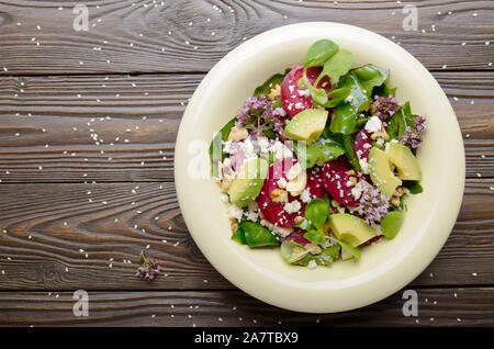 Vista superiore al mediterraneo barbabietole arrosto con insalata di avocado noci e formaggio feta origano e mash lascia sul tavolo di legno Foto Stock