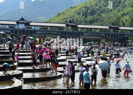 I visitatori un tuffo per rinfrescarsi in acqua in una posizione nota per il pesce in scala barriere sagomati che formano piccole cascate nel quartiere Fuyang, Hangzhou ci Foto Stock