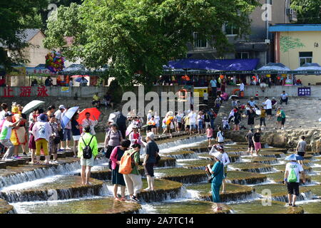 I visitatori un tuffo per rinfrescarsi in acqua in una posizione nota per il pesce in scala barriere sagomati che formano piccole cascate nel quartiere Fuyang, Hangzhou ci Foto Stock