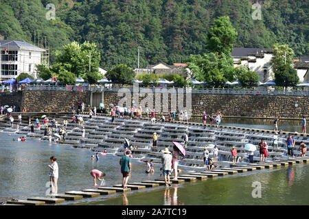 I visitatori un tuffo per rinfrescarsi in acqua in una posizione nota per il pesce in scala barriere sagomati che formano piccole cascate nel quartiere Fuyang, Hangzhou ci Foto Stock