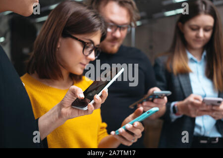 Un gruppo di giovani persone positive stand in linea con i moderni smartphone. Adulto team aziendale utilizzando mani telefono. Riunione di concetto Foto Stock