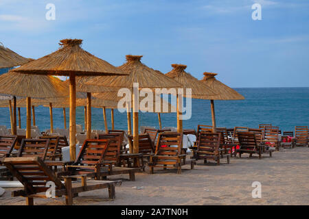 Sedie a sdraio e ombrelloni di paglia sul resort tropicale. La linea di sedie a sdraio. Il blu del mare e del cielo su sfondo. Vacanze estive concetto. Foto Stock