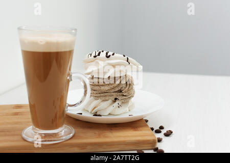 French vanilla meringue cookies con crema per il caffè e un bicchiere di latte su sfondo bianco. Foto Stock
