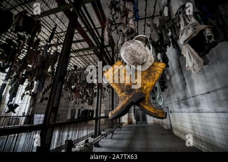 Giallo stivali di gomma e un casco in una vecchia catena di data mining spogliatoio presso il Parco Landek Museum, Ostrava, Repubblica Ceca. Foto Stock