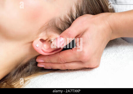 In prossimità di un lato femminile di estetista toccando donna le orecchie e templi testa facendo un massaggio nel centro benessere salone di bellezza. Foto Stock