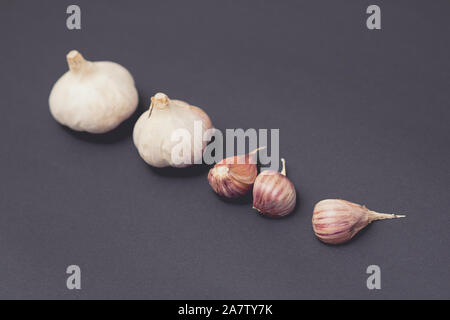 Testa di aglio e chiodi di garofano di aglio disposti in una fila sulla superficie nera. Foto Stock