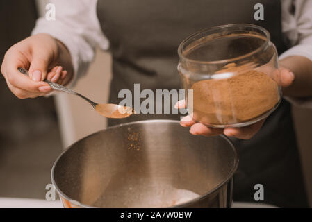 Il cuoco ragazza riversa marrone zucchero di canna in una ciotola di metallo. La cottura di dolci in cucina Foto Stock