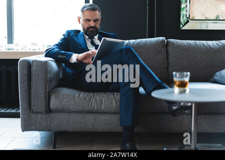 Bel giovane uomo che lavora con il computer portatile mentre è seduto sul divano in office Foto Stock