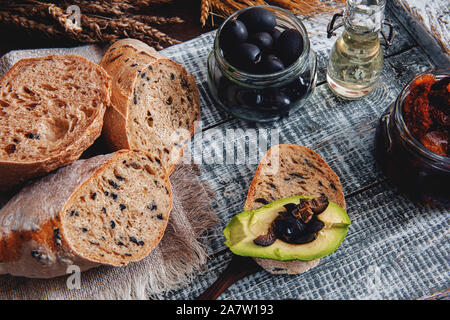 Una sana segale pane integrale con olive, avocado e pomodori secchi su una tavola di legno dell'agricoltore tabella. Torte fatte in casa.La tradizionale cucina italiana. Foto Stock