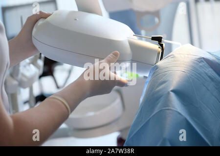 Il dentista imposta una macchina a raggi X per una fotografia di controllo dei denti del paziente Foto Stock