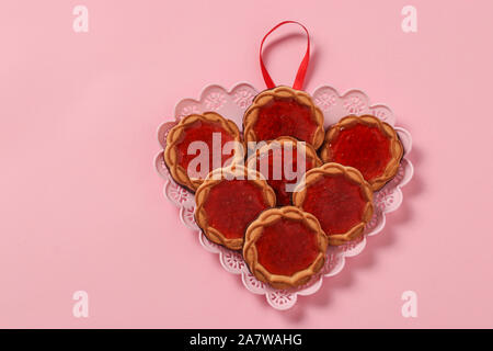 I biscotti con marmellata di frutti di bosco su di una piastra a forma di cuore per il giorno di San Valentino su uno sfondo rosa Foto Stock