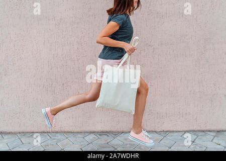 Donna rosa in pantaloncini corti e scarpe da ginnastica è il salto con cotone bianco borsa nelle sue mani. Foto Stock