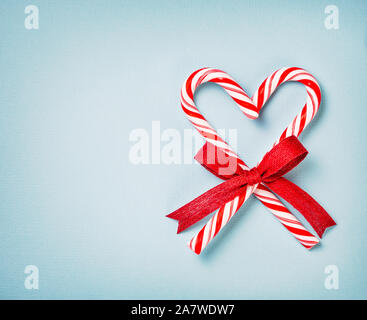 Natale Candy Canes cuore avvolto in un arco su una luce blu carta testurizzata sfondo. Foto Stock