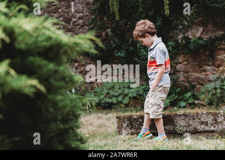 Vista laterale del ragazzo in piedi in giardino contro il muro di pietra Foto Stock