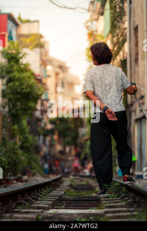 Una donna locale vive sulla famosa in tutto il mondo via treno ad Hanoi, Vietnam acque le piante e il suo giardino come turisti a piedi da Foto Stock