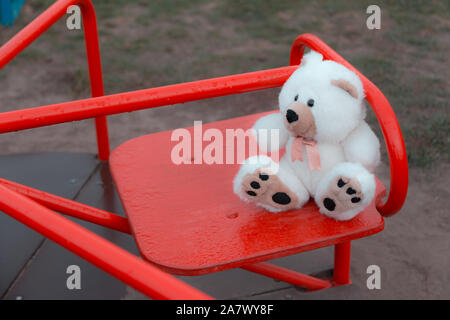 Close-up un orsacchiotto è seduta su di un bambini swing in rosso. Il concetto di tristezza, perdita, morte, lutto, orphanhood o solitudine Foto Stock