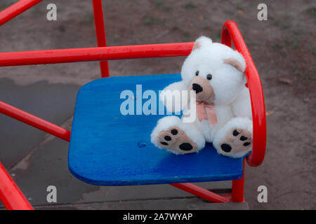 Close-up un orsacchiotto è seduta su di un bambini swing in rosso. Il concetto di tristezza, perdita, morte, lutto, orphanhood o solitudine Foto Stock