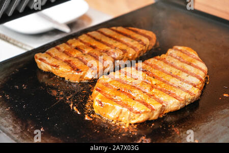 Due bistecche di maiale alla griglia su griglia elettrica, piastra di metallo Foto Stock