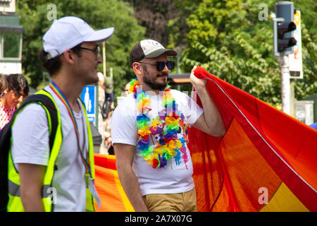 Malmö, Svezia - 20 Luglio 2019: Un uomo barbuto con occhiali da sole e cappello da baseball sta portando una grande bandiera banner come egli partecipa al Gay Pride Parade Foto Stock