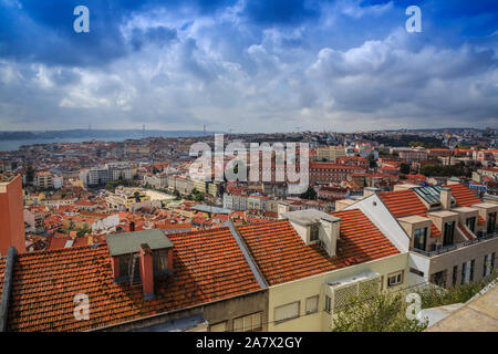 Miradouro da Graca vista del sud-ovest di Lisbona, Portogallo, come il suo rosso-tile ampiezza raggiunge il ponte di Alcantara e orizzonte sotto un cielo drammatico. Foto Stock