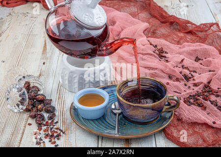 Il tè di rosa canina: Processo di preparazione del tè,la cerimonia del tè, la tazza di appena infuso di tè di rosa canina su uno sfondo di legno. Foto Stock