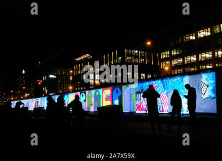 Berlino, Germania. 04 Nov, 2019. I visitatori a guardare il video installazione presso la East Side Gallery nel buio. In occasione della celebrazione del trentesimo anniversario della caduta del muro di Berlino, questo sarà illuminato da uno show multimediale. Credito: Annette Riedl/dpa/Alamy Live News Foto Stock