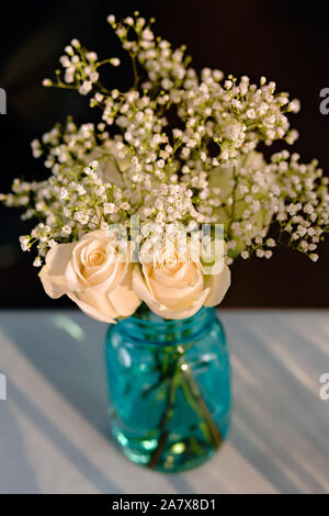 Bouquet di rose bianche e NEONATI il respiro dei fiori in un blu vaso di vetro su una tovaglia bianca ad un ricevimento di nozze Foto Stock
