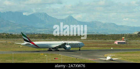 Emirates Airline Boeing 777 volo commerciale sulla pista di Cape Town International Airport contro uno sfondo di montagne Foto Stock